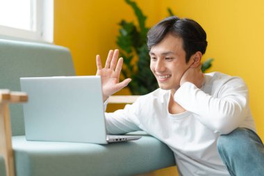 Asyalı bir adam yerde oturmuş video görüşmesi yapıyor.