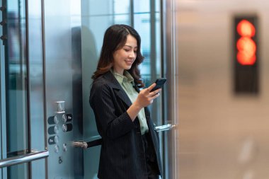 Asansörde duran ve telefon kullanan genç iş kadınının portresi.
