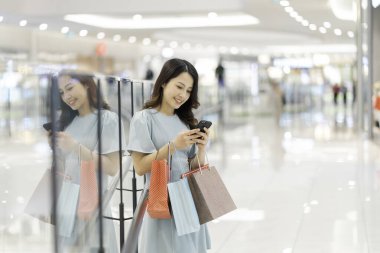 Genç kız alışveriş merkezinde telefonu kullanıyor.