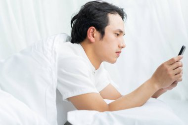 Genç adam yatağında telefonla yatıyor.