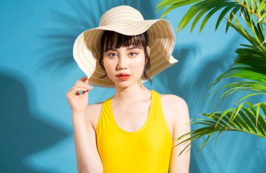 Mavi arka planda sarı tulum giyen güzel Asyalı kadın ve yaz konsepti.