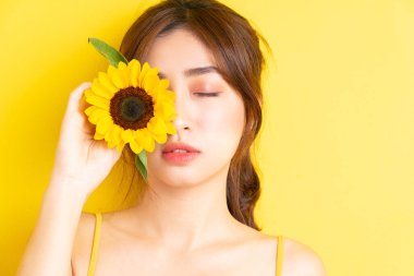 Sarı arka planda ayçiçeğiyle poz veren güzel Asyalı kadın