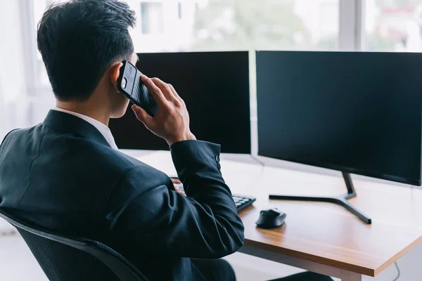 Asian business people are focused on working while on the phone. A computer with two blank screens