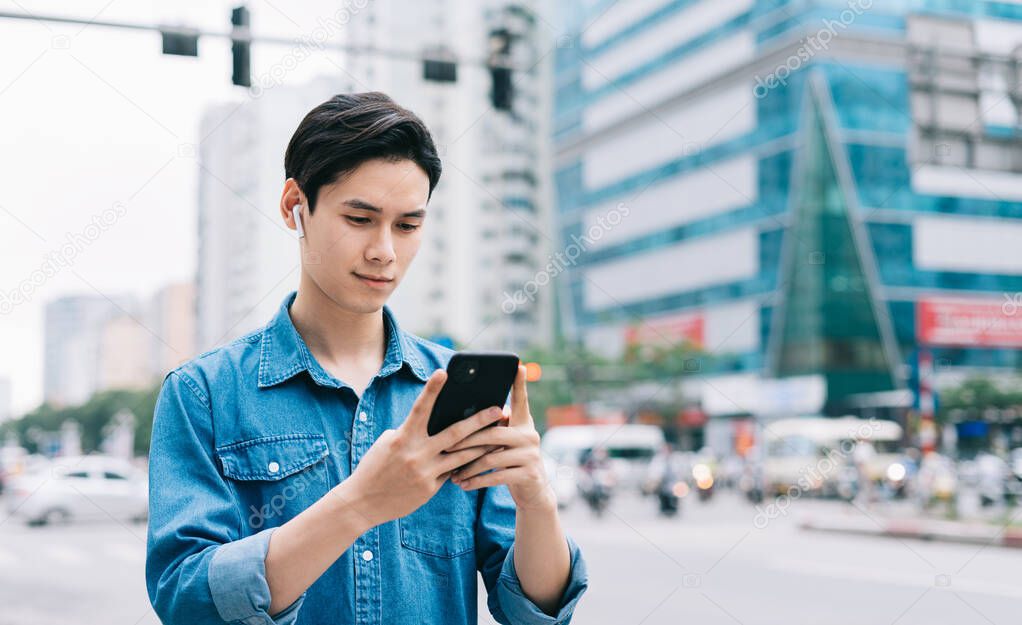 Young Asian man walking and using smartphone on the street