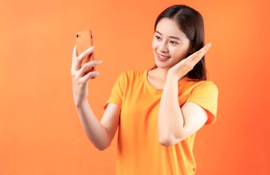 Turuncu arka planda akıllı telefon tutan Asyalı genç bir kadın resmi