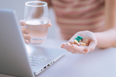 Young Asian woman holding cup of water and medicine in hand to prepare for use