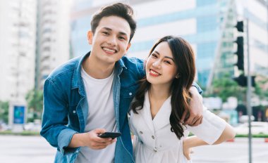 Genç Asyalı çift sokakta birlikte akıllı telefon kullanıyor.