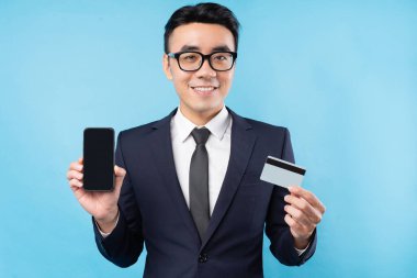 Akıllı telefon ve banka kartı tutan takım elbiseli bir Asyalı.