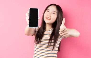 Genç Asyalı kadın pembe arka planda akıllı telefon kullanıyor.