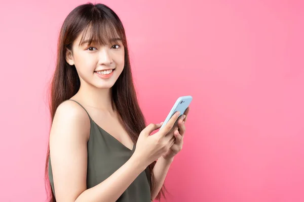 분홍색 배경으로 핸드폰을 사용하는 아리따운 아시아 — 스톡 사진