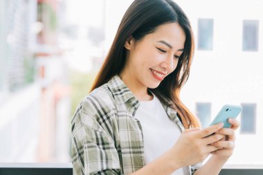 Evde akıllı telefon kullanan Asyalı genç bir kadının portresi