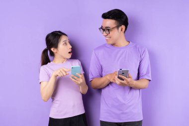 Genç Asyalı çift mor arka planda akıllı telefon kullanıyor