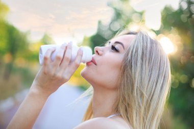 Beyaz bir şişeden içen genç sarışın bir kadın. 