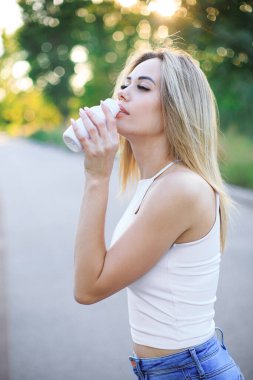 Beyaz bir şişeden içen genç sarışın bir kadın. 