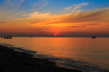 Güneş, deniz koyunun üstündeki dağın arkasından doğuyor.