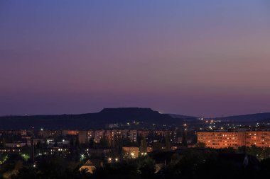 Dağlık bölgede fenerleri olan şehir. Gün batımı veya şafak vakti gökyüzü olan.
