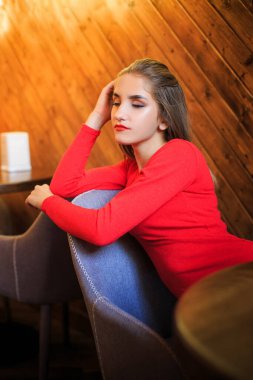 Bir kafede sandalyede oturan kırmızılı genç bir kadının portresi.