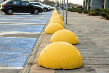 Alışveriş merkezinin yanındaki kaldırımda sarı park önleyici yarımküreler var.