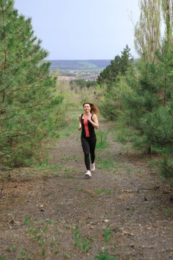 A young woman does a running workout in a coniferous forest