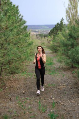 A young woman does a running workout in a coniferous forest
