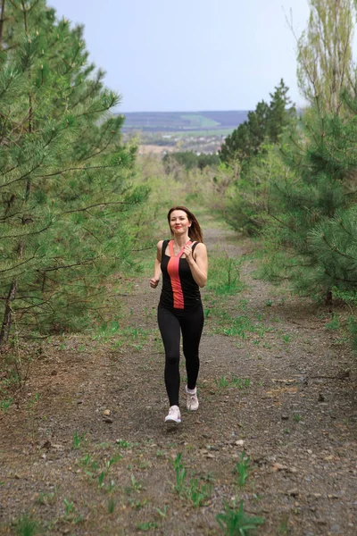 A young woman does a running workout in a coniferous forest
