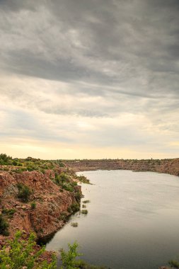 Bulutlu bir günde eski bir kırmızı granit ocağının kıyıları suyla doldu..