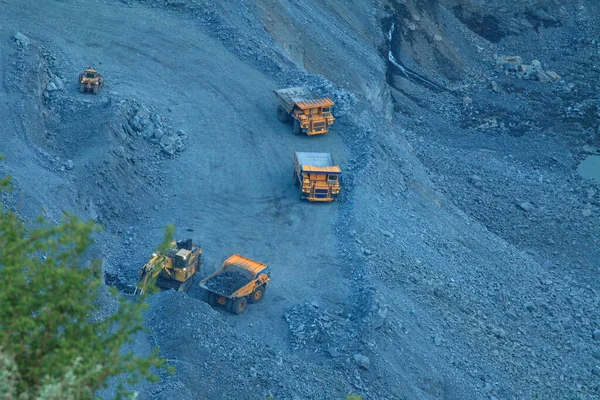 The process of mining iron ore in a quarry with large excavators and trucks. Heavy iron ore mining industry at night