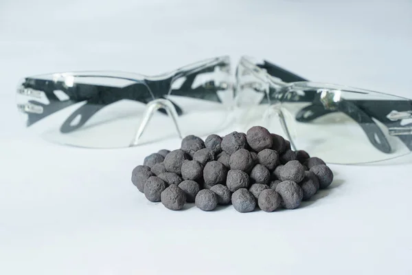 Iron ore pellets on white background, safety glasses in the background. Finished raw material for metallurgy iron ore granules