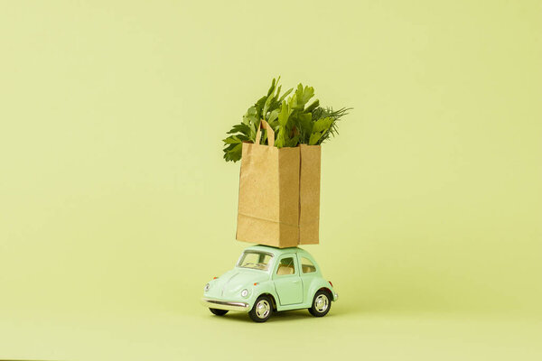Irkutsk, Russia - October 3, 2020: Light green retro toy car carries paper shopping bags with fresh green salad. Eco foods delivery concept, vegetarianism. Donation.