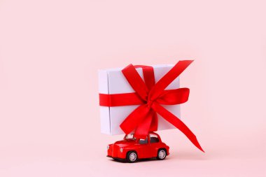 Sevgililer günü, yeni yıl, küçük kırmızı eski oyuncak araba çatıda büyük bir hediye ve pembe arka plan. Dünya Kadınlar Günü 'nde Noel için hediyeler getirdim. Satış konsepti. Yakın plan..
