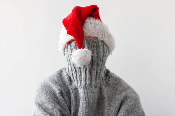 A teenage girl in a Santa hat pulled the collar of her sweater over her face. New years concept in isolation — Stock Photo, Image