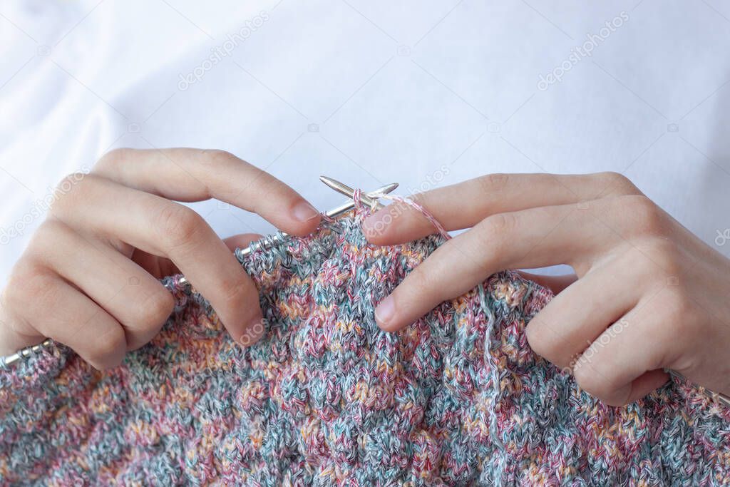 Two hands on a white background hold knitting needles and knitting close-up . The concept of hand made, home, Hobbies.