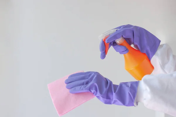 Dos manos en guantes de goma, una sosteniendo un paño de tratamiento superficial, la otra una botella de spray naranja. Concepto de limpieza, limpieza, nueva realidad, tratamiento de superficies — Foto de Stock