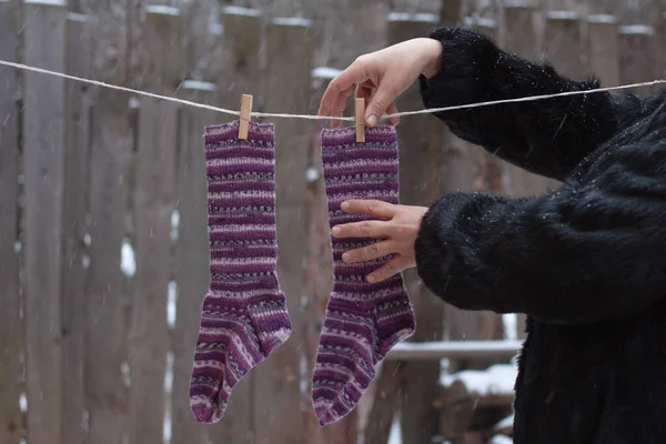 Calcetines de lana cuelgan de una cuerda con pinzas de ropa, las manos de las mujeres se quitan los calcetines, está nevando. En invierno, seque su ropa afuera y manténgalos calientes. — Foto de Stock