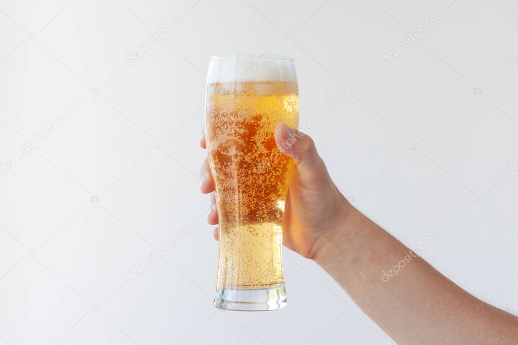 A hand holds a full glass of light beer with bubbles and foam on a white background.