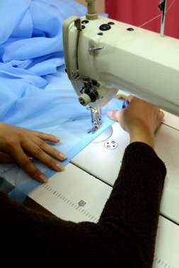 Terzi dikiş makinesine dikiş dikiyor, siparişi yerine getiriyor. Mavi bir bez karalıyor. Perde dikiyorum. Küçük işletme.