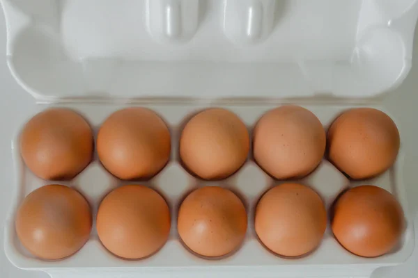 An open egg carton with ten brown eggs, on white background. Top view of egg container, fresh organic chicken eggs.
