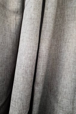 Yoğun kumaştan ince ve kalın dikey kıvrımlı gri perdelerin yakın çekimi. Soyut arka planlar ve duvar kağıtları. Keten kumaşlar.