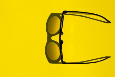 Sarı arka planda siyah gözlükler var, kopyalama alanı. Sert güneş ışığı ve düz yatış, tatil ve seyahat kavramı