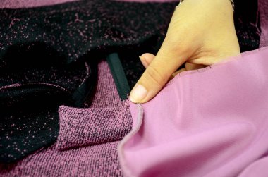 Terzi elbise dikmek için örgü hazırlar. Kadın elleri dikiş masasında siyah ve pembe bir kumaş tutuyor. Küçük bir iş. Seçici odak.