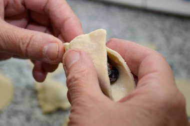 Yağsız hamur tatlısı modelliği. Kadın elleri hamuru böğürtlenlerle çimdikliyor. Bir kadın Ukrayna ulusal yemeğini hazırlıyor. Seçici odak.