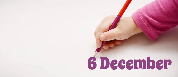 A child\'s hand writes December 6 in lilac pencil. Banner with copy space. Important date concept