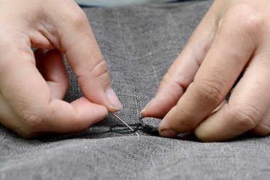 Female hands with a needle with a black thread sew a gray button to the furniture upholstery, horizontal photo. Small business concept.
