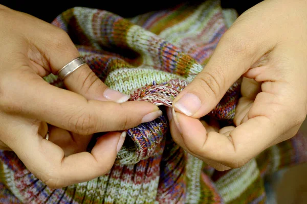 Women\'s hands crochet a sweater. The color knitted sweater is torn. Selective focus.