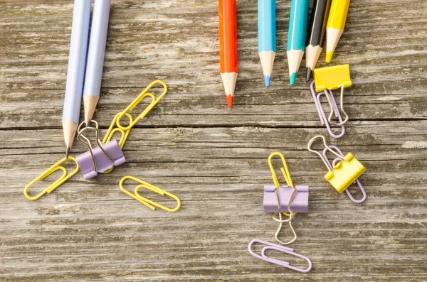 Office supplies colored pencils and paper clips wooden background