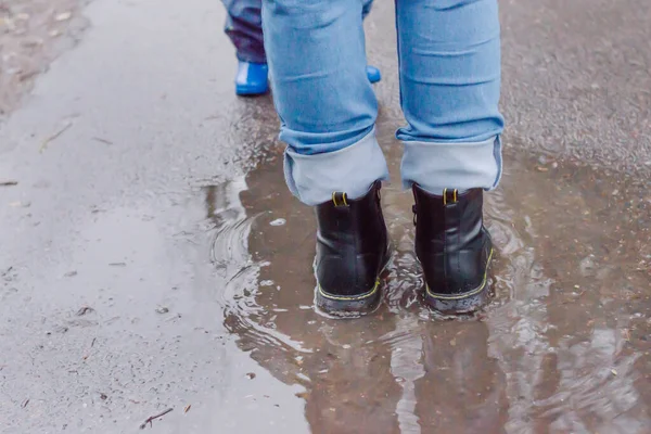 Legs of young woman in blue jeans and shoes stand in a puddle on the asphalt