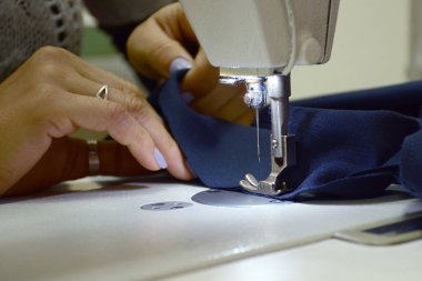 Dikiş makinesine dikiş dikmek bir emri yerine getirir. Mavi bir bez karalıyor. Küçük işletme.