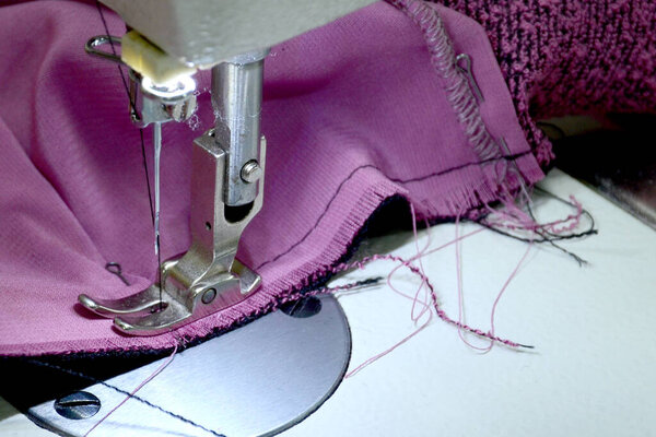 Sewing pink knitwear on a white sewing machine. Small business concept. Selective focus.