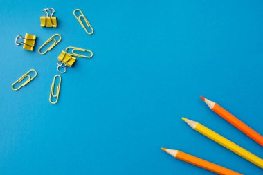 Mavi arka planda ataçlı turuncu ve sarı kalemler, düz. Boş kopyalama alanı