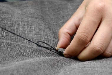 Siyah iplikli bir terzi gri bir kumaş düğmesine diker, yatay bir fotoğraf. Küçük işletme kavramı.